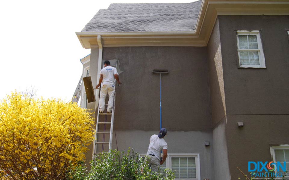 Two men using a ladder to paint the exterior of a house