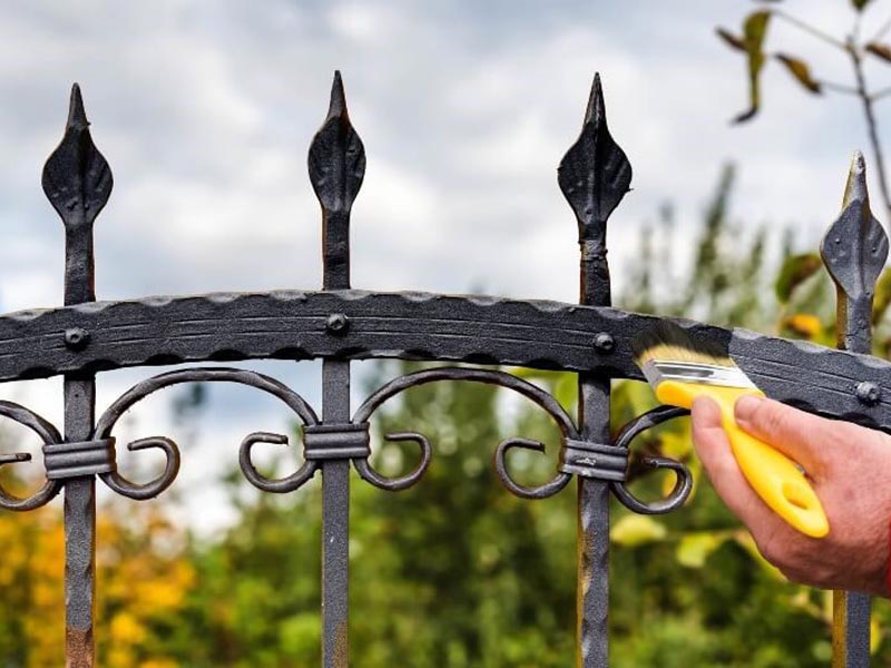 man painting a wrought iron fence