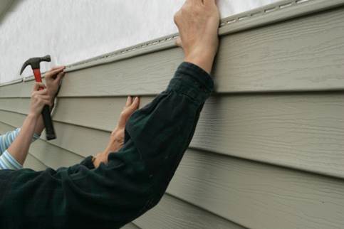 A man installs siding on a house using a hammer