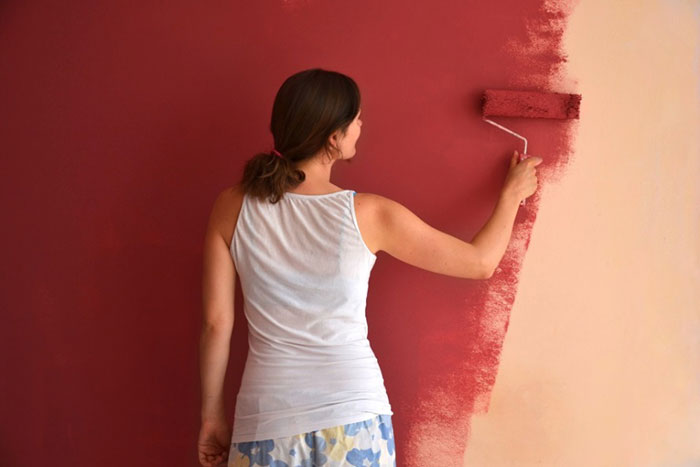 A woman applies red paint to a wall