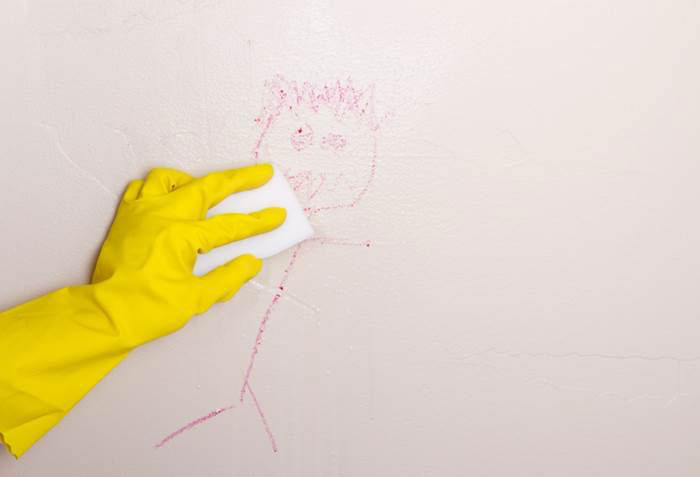 A person with rubber gloves is seen cleaning a wall that displays a child's drawing