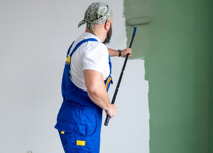 A man dressed in overalls paints a green wall